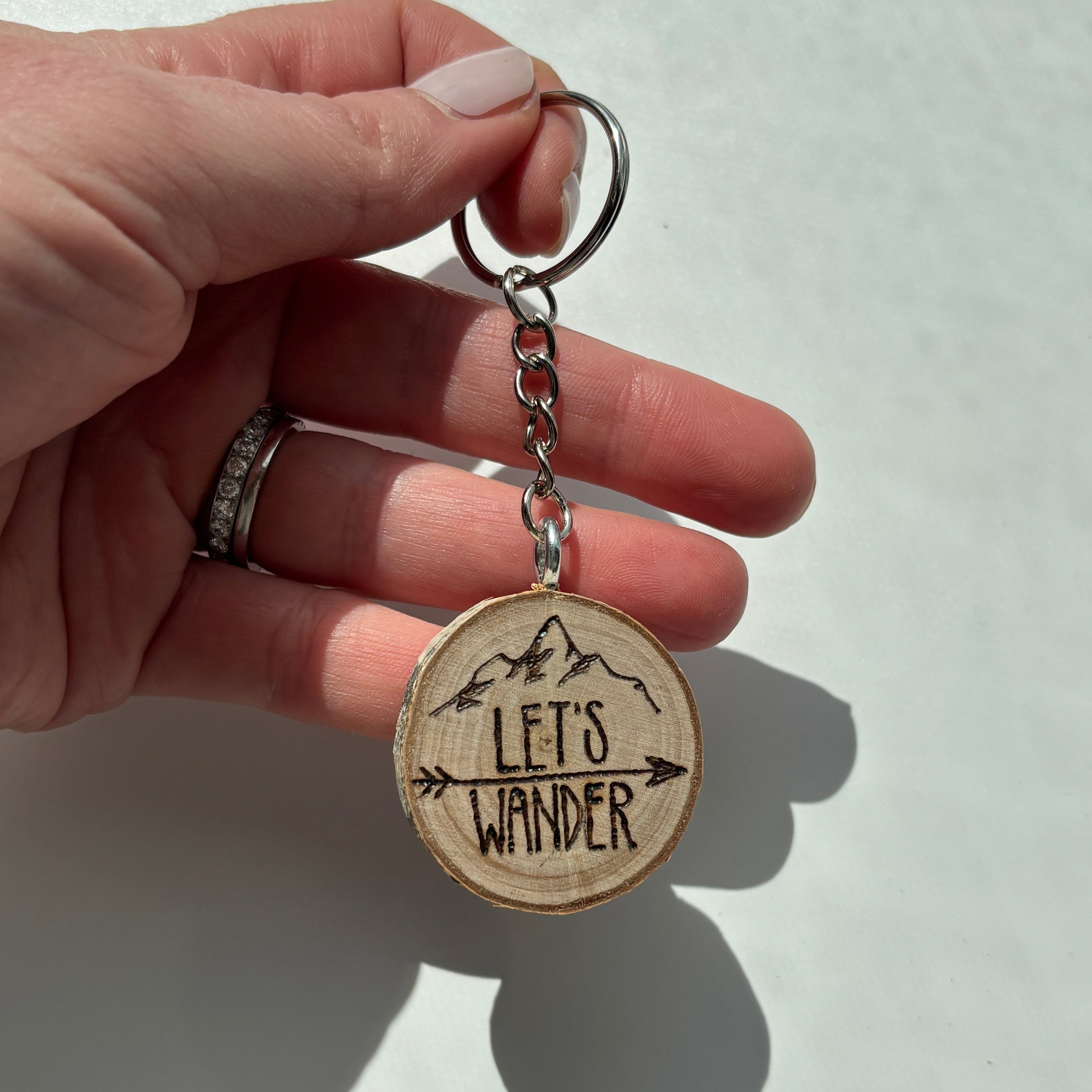 Hand holding a keychain with 'Let's Wander' engraving on a light background