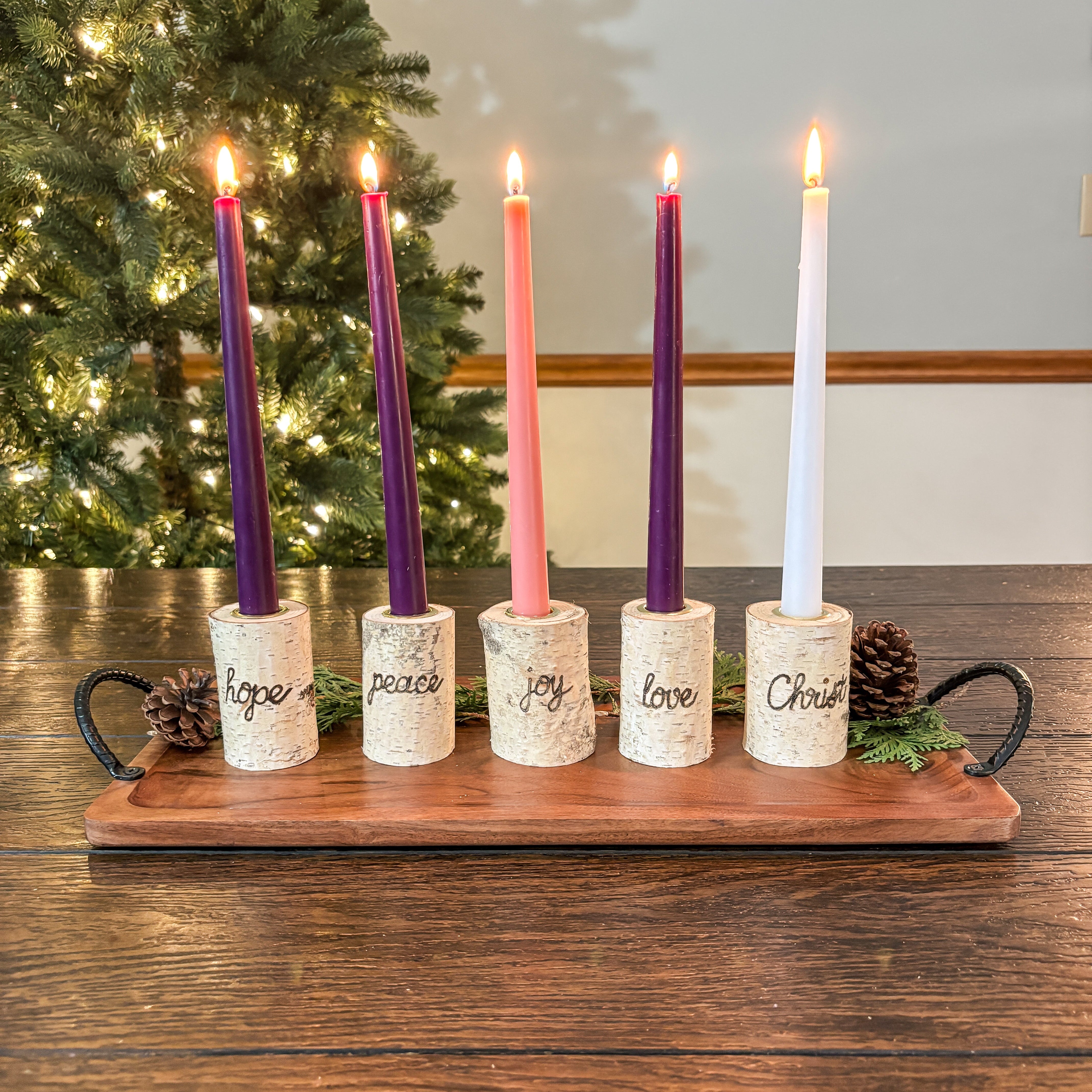Set of Advent candles with wooden holder in front of a Christmas tree.