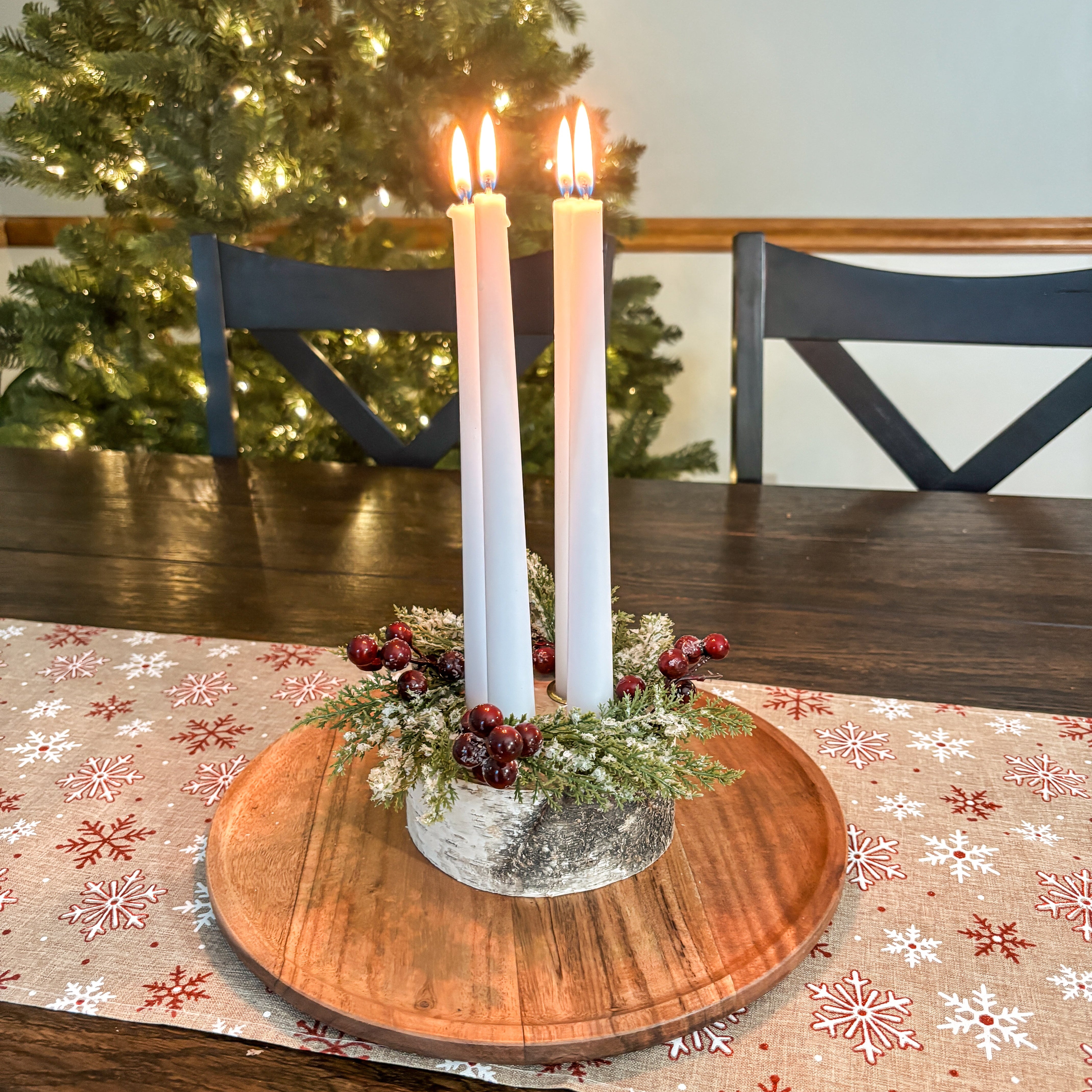 Decorative candle holder with candles on a wooden table in front of a Christmas tree.