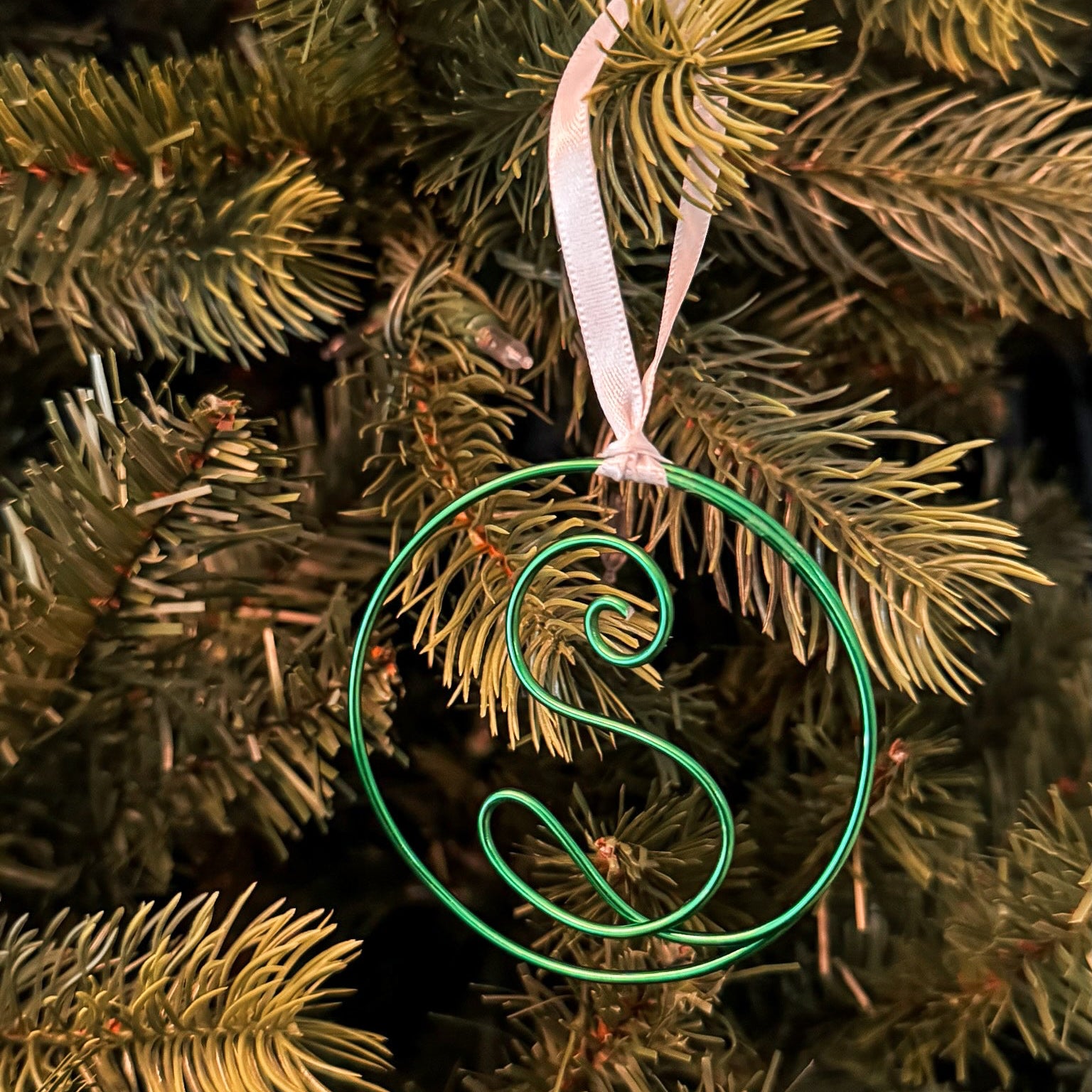 Decorative green letter 'S' ornament on a Christmas tree