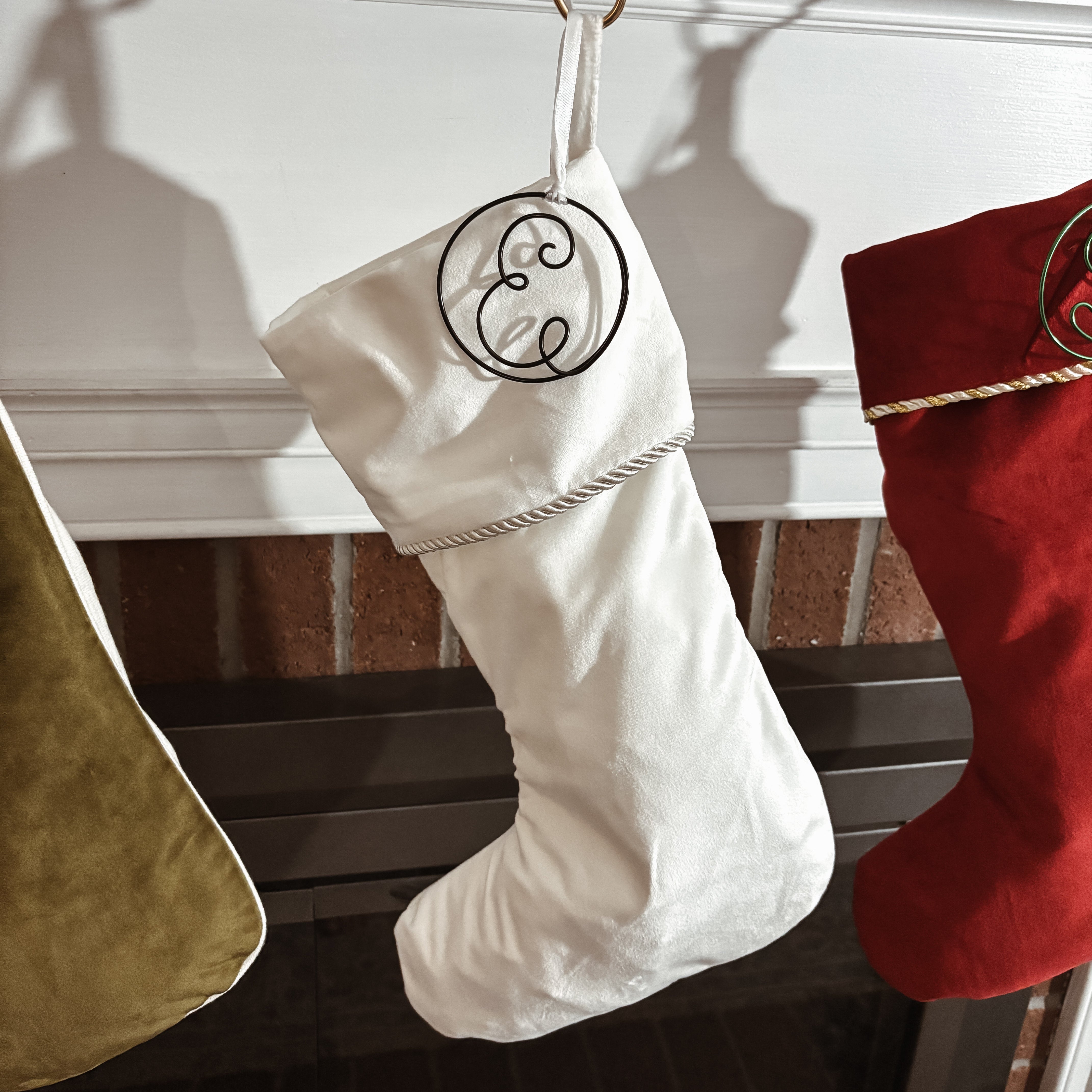 White Christmas stocking with a decorative 'E' hanging on a fireplace mantle.