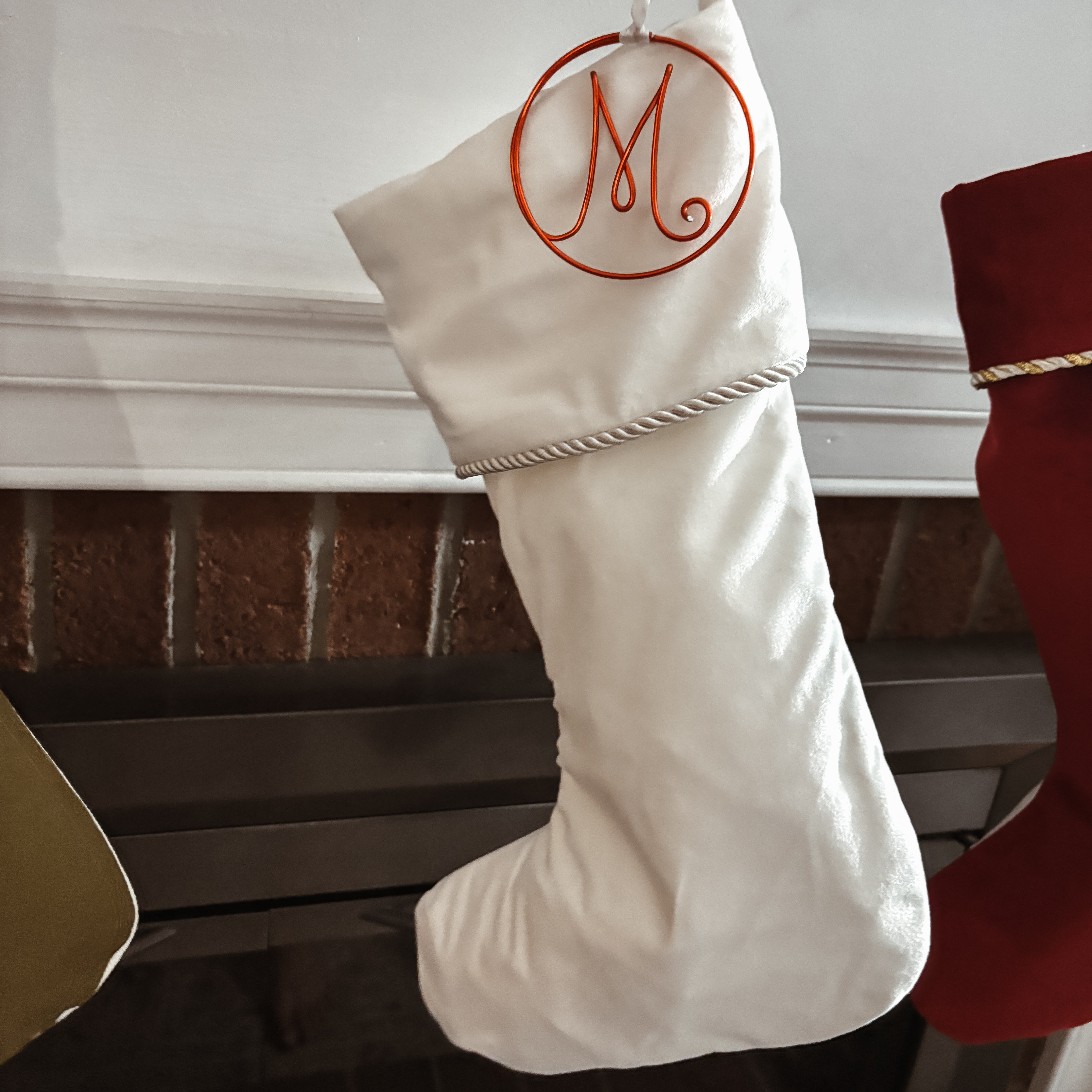 White Christmas stocking with a red 'M' monogram hanging on a fireplace.