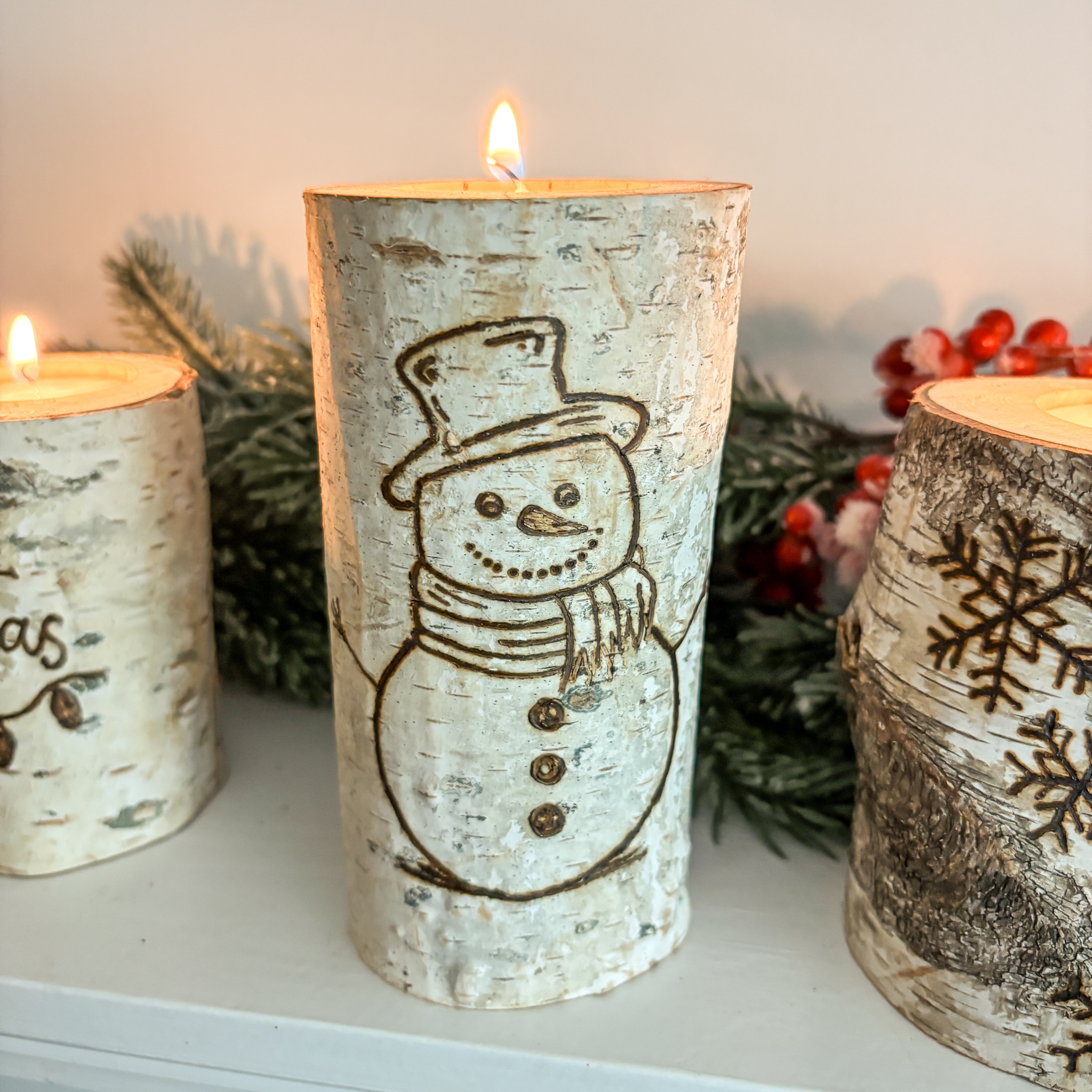Decorative candles with snowman and winter designs on a white surface.