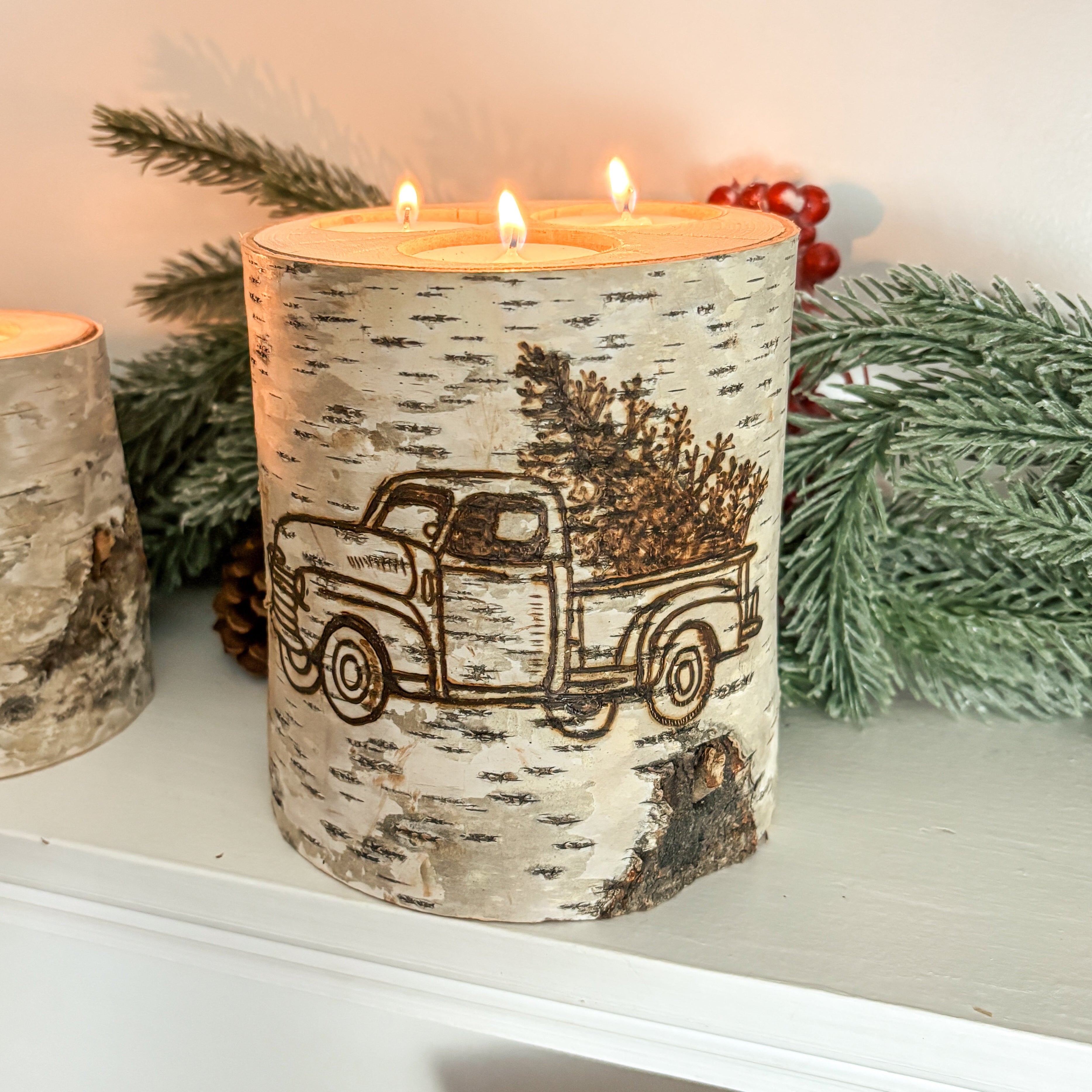 Decorative candles with a truck design on a mantelpiece with Christmas decor.