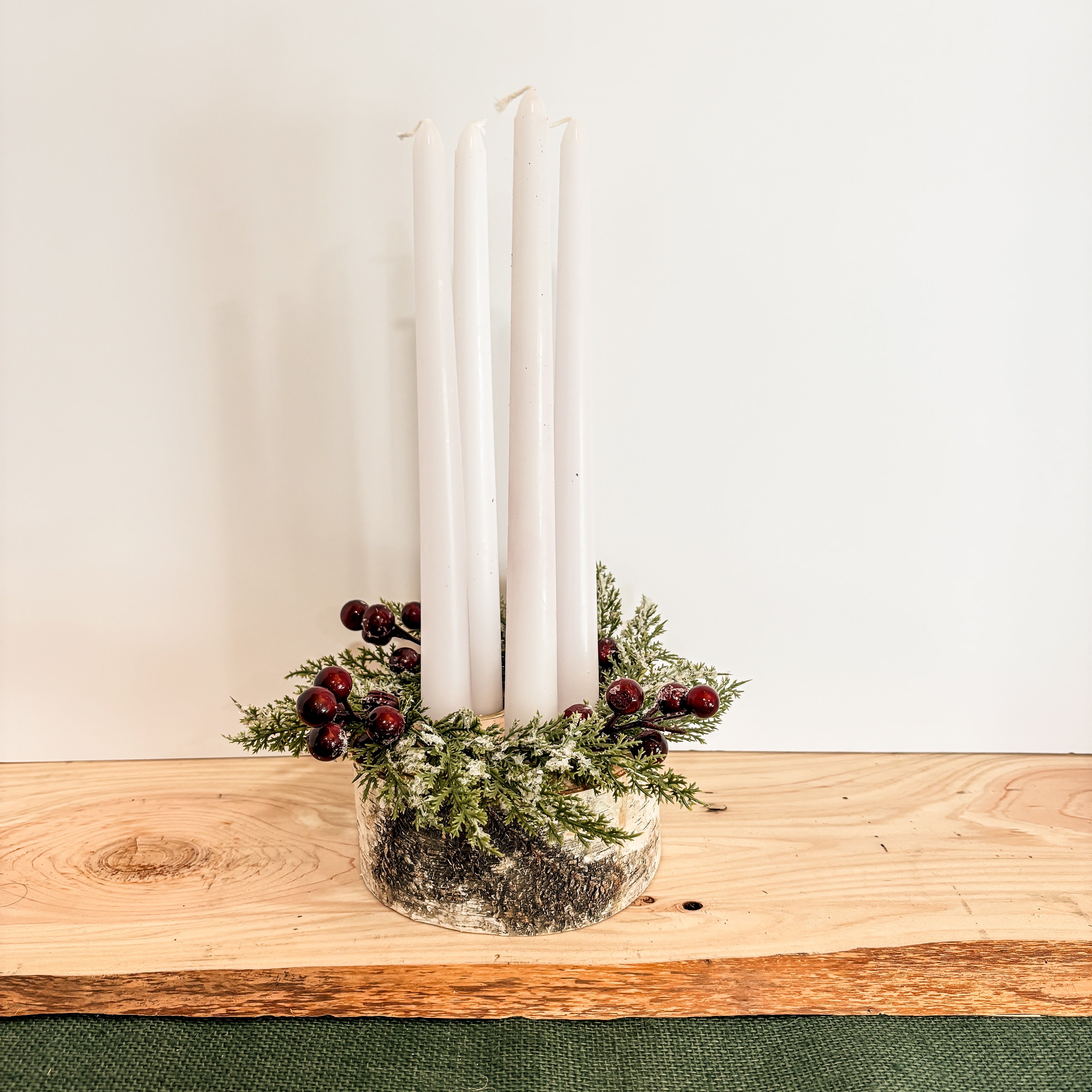 Decorative birch wood Christmas taper candle holder centerpiece with holiday greenery and candles on a wooden surface