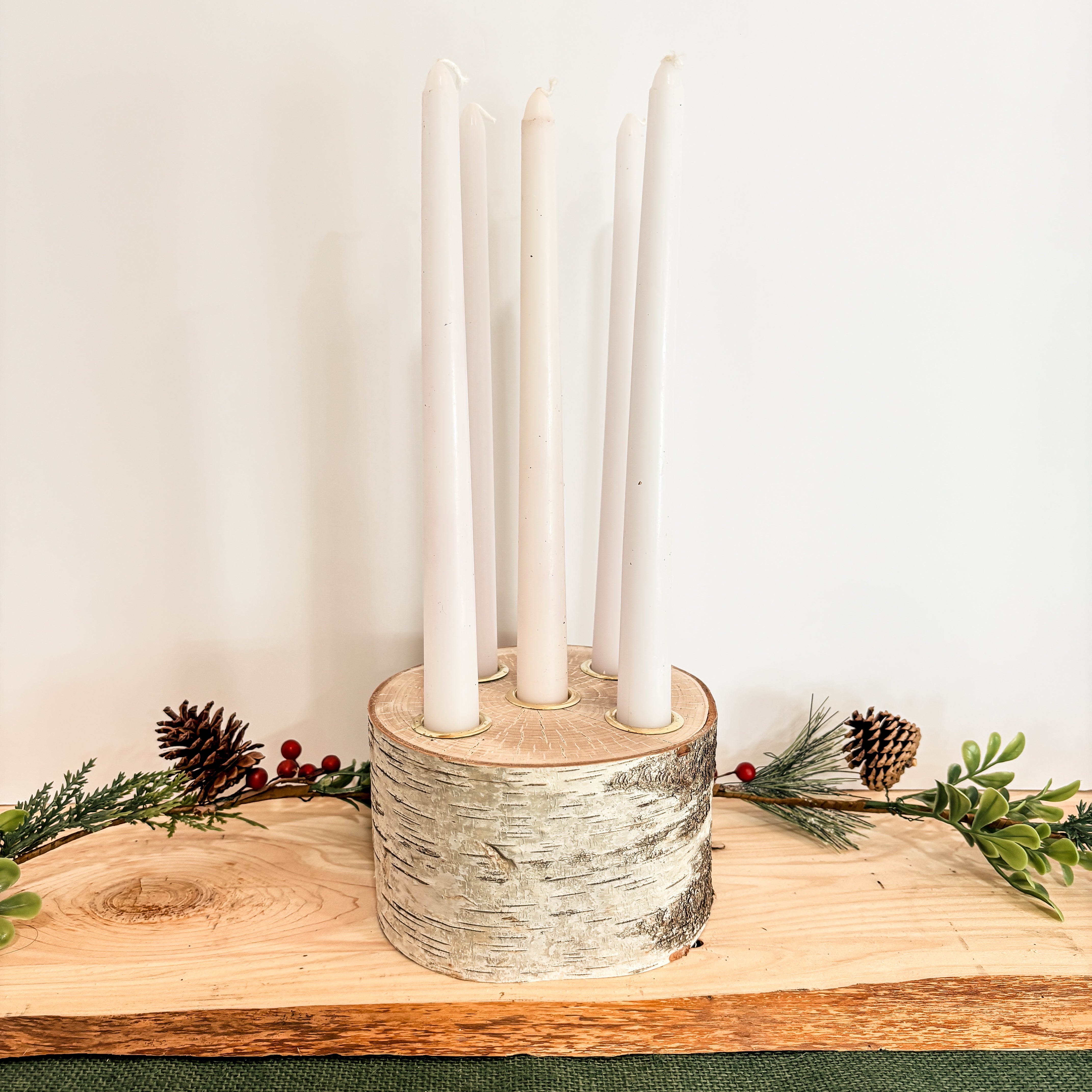 Candle holder with five white candles on a wooden surface with greenery and pinecones perfect for a Christmas table centerpiece 