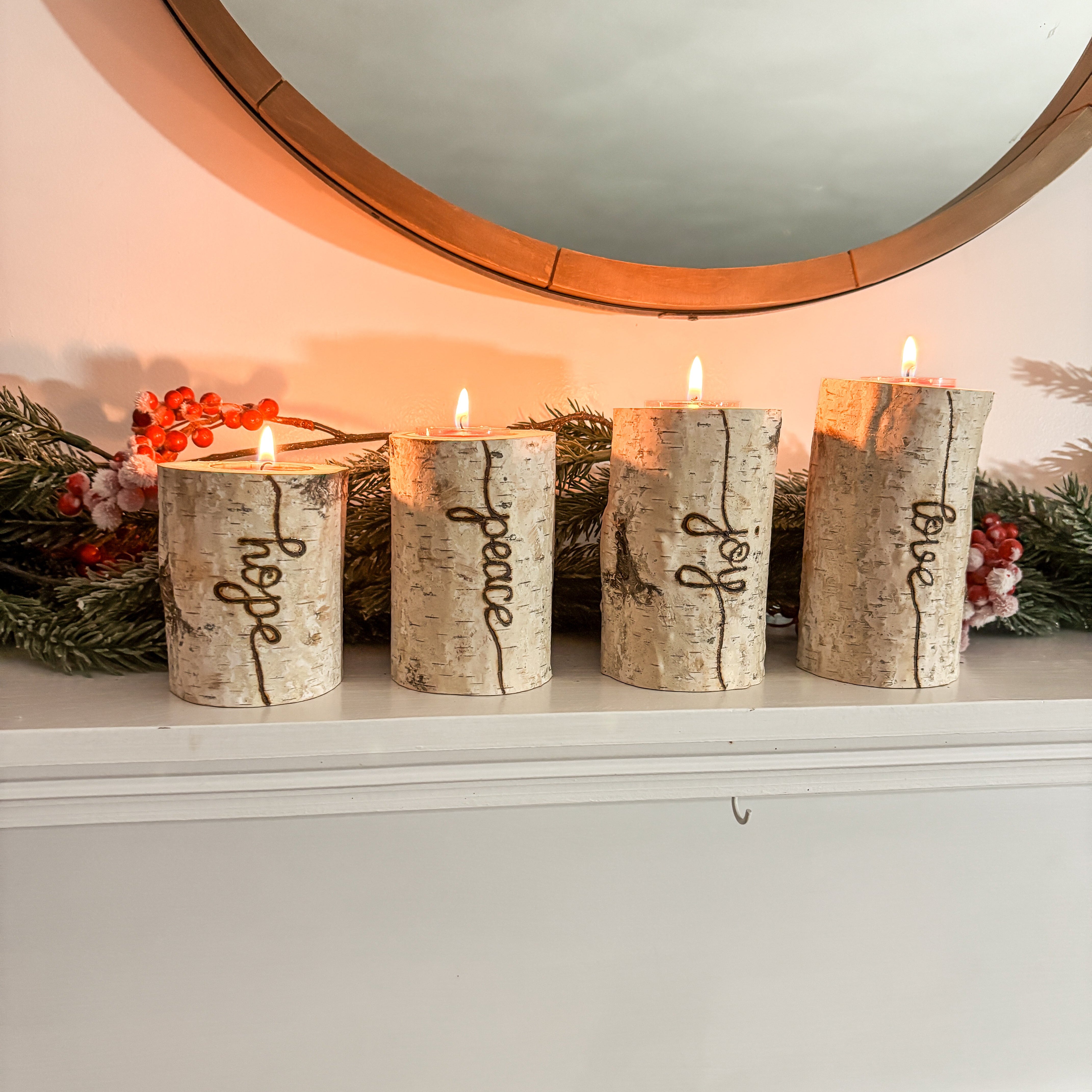 Decorative candles with engraved words on a mantelpiece with a mirror in the background.