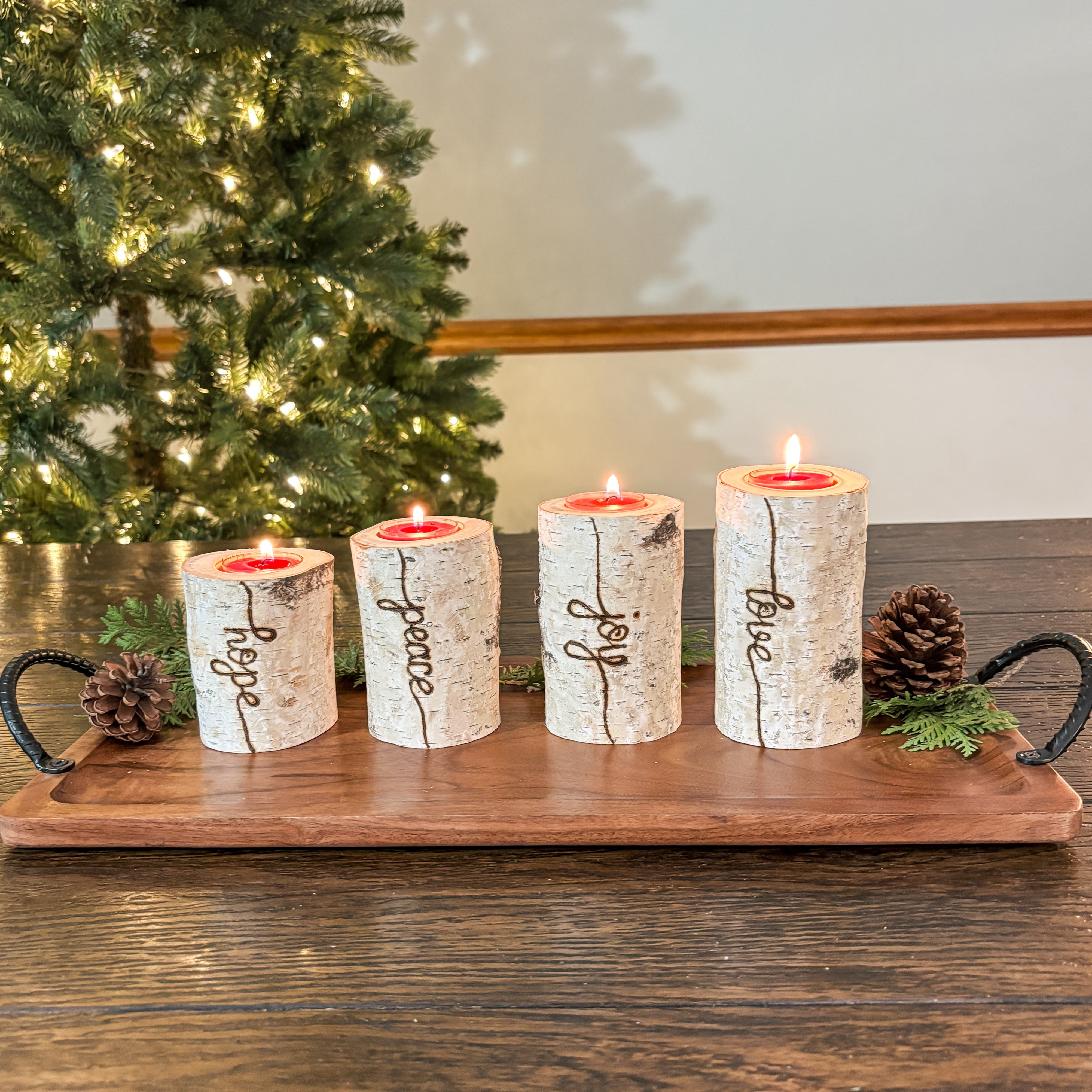 Decorative candles on a wooden tray with a Christmas tree in the background