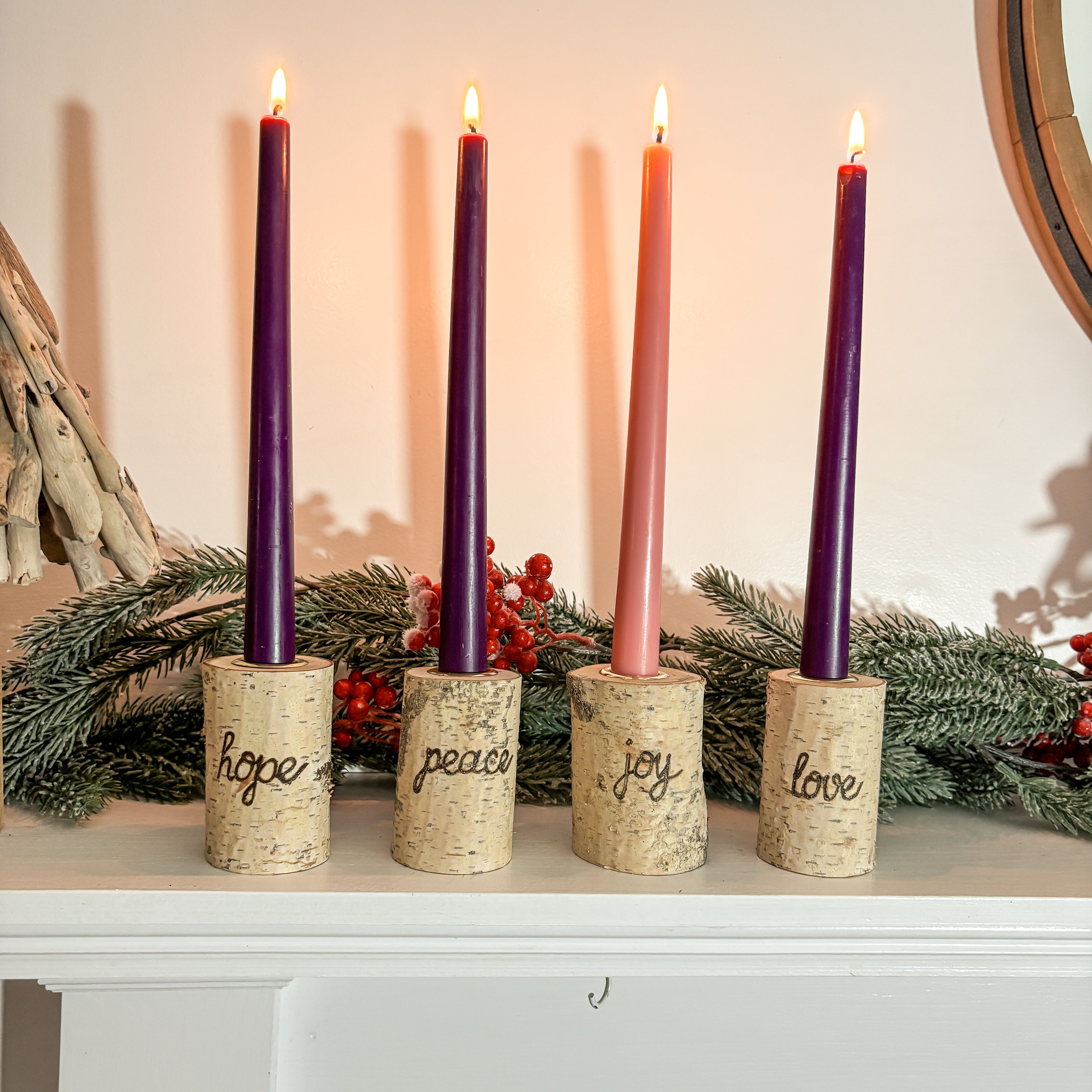 Five Advent candles with labels 'hope', 'peace', 'joy', 'love' on a white surface with a festive background.