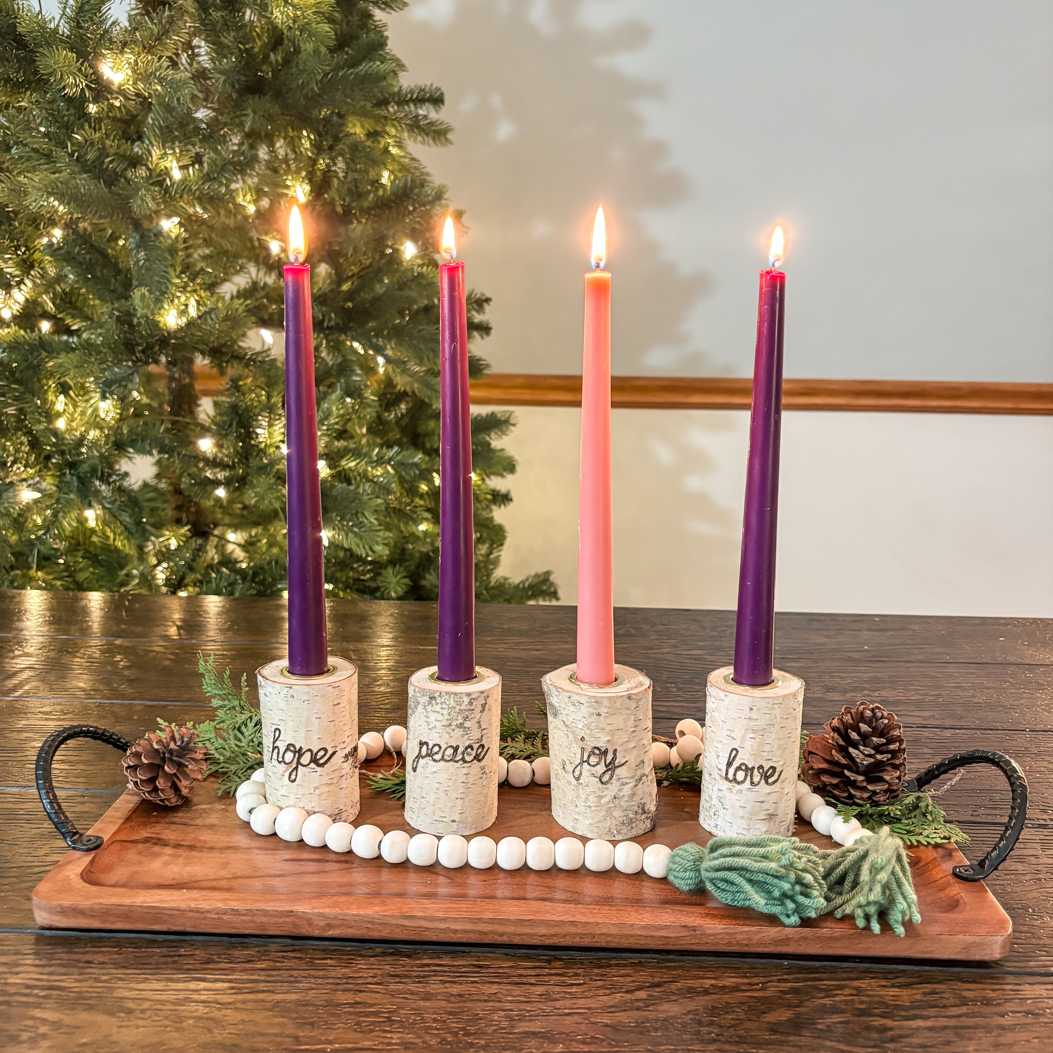 Advent candle holder with lit candles in front of a Christmas tree.