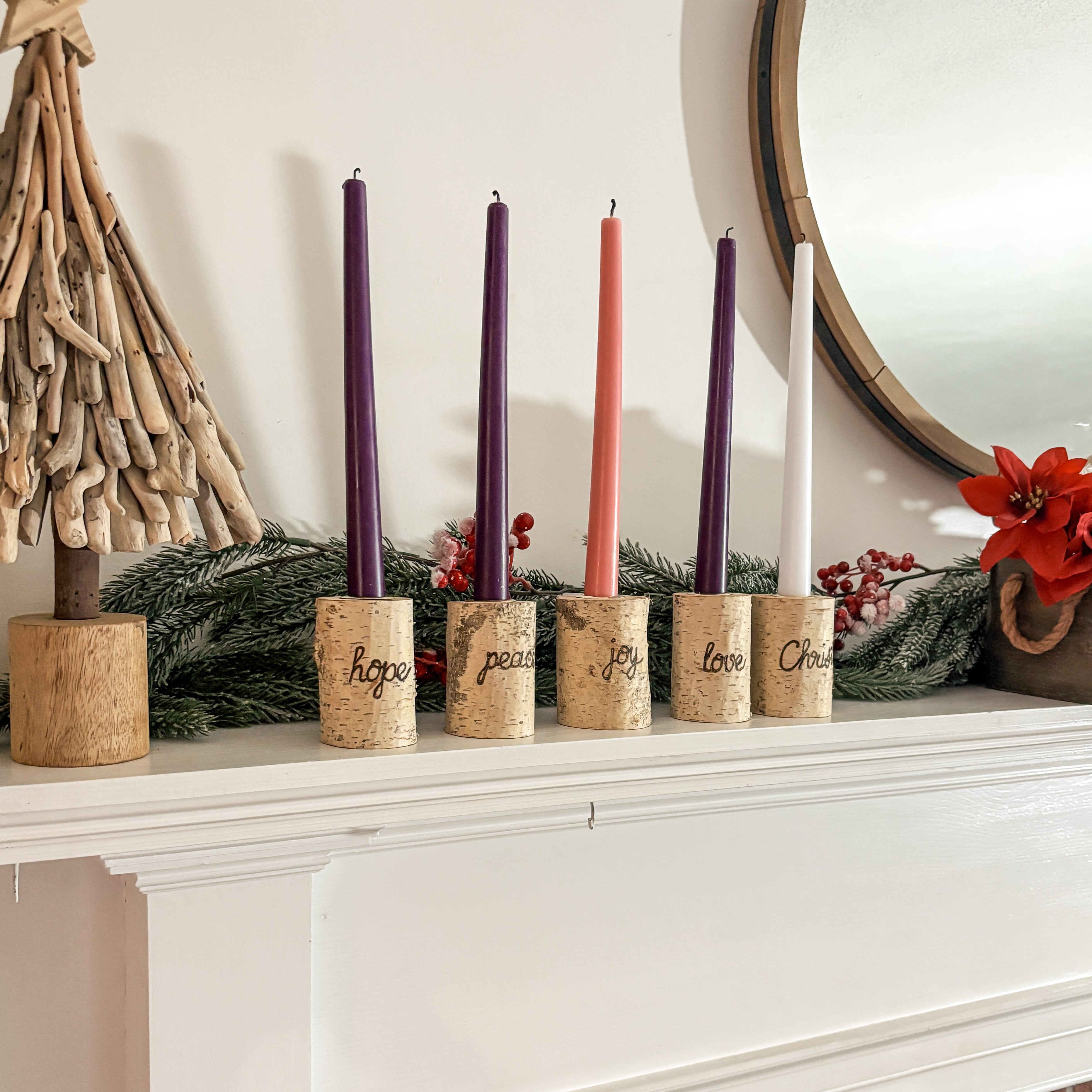 Decorative candles on a mantelpiece with a small tree and mirror in the background.