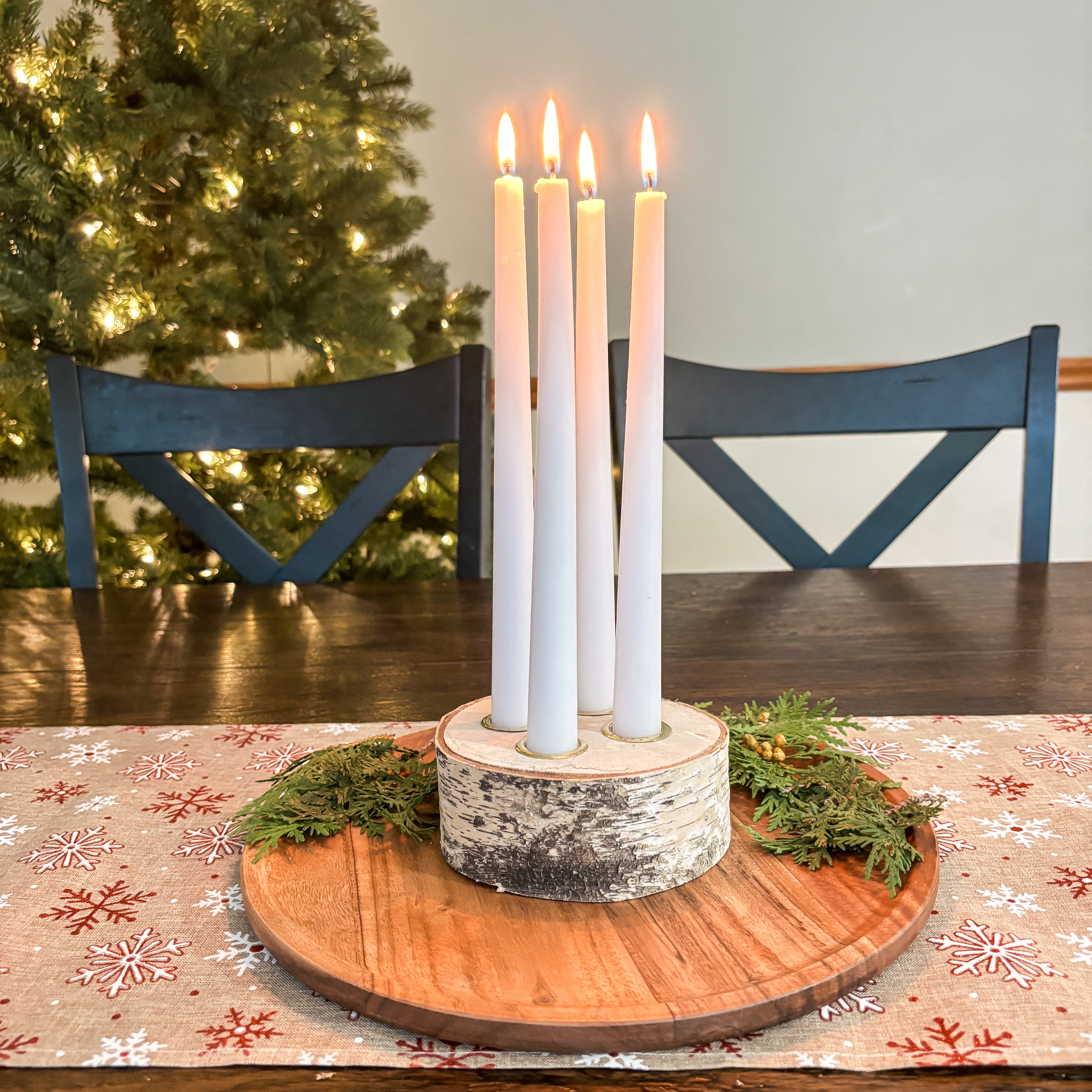 Wooden candle holder with five lit candles on a table in front of a Christmas tree.