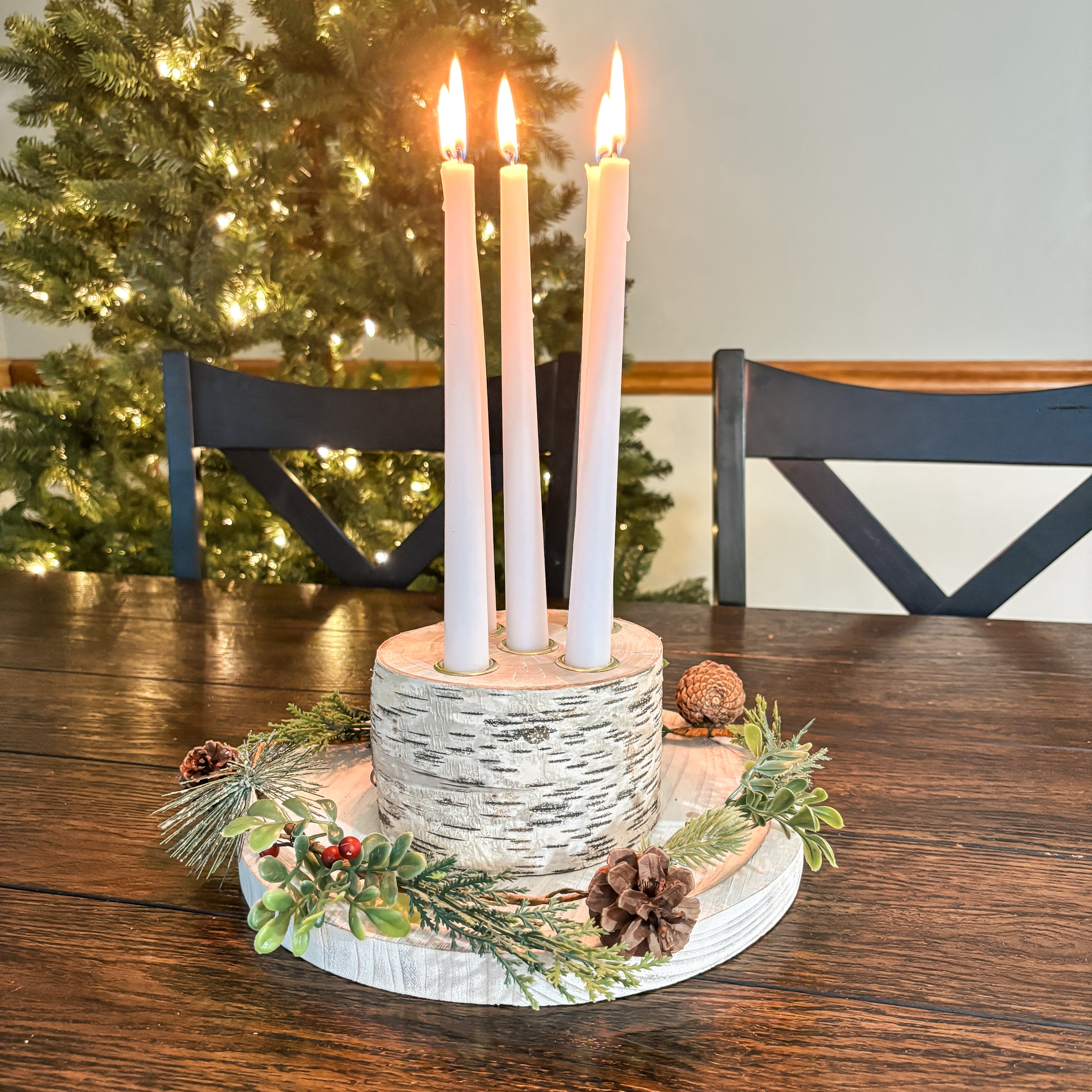 Decorative candle holder with lit candles on a wooden table in front of a Christmas tree.