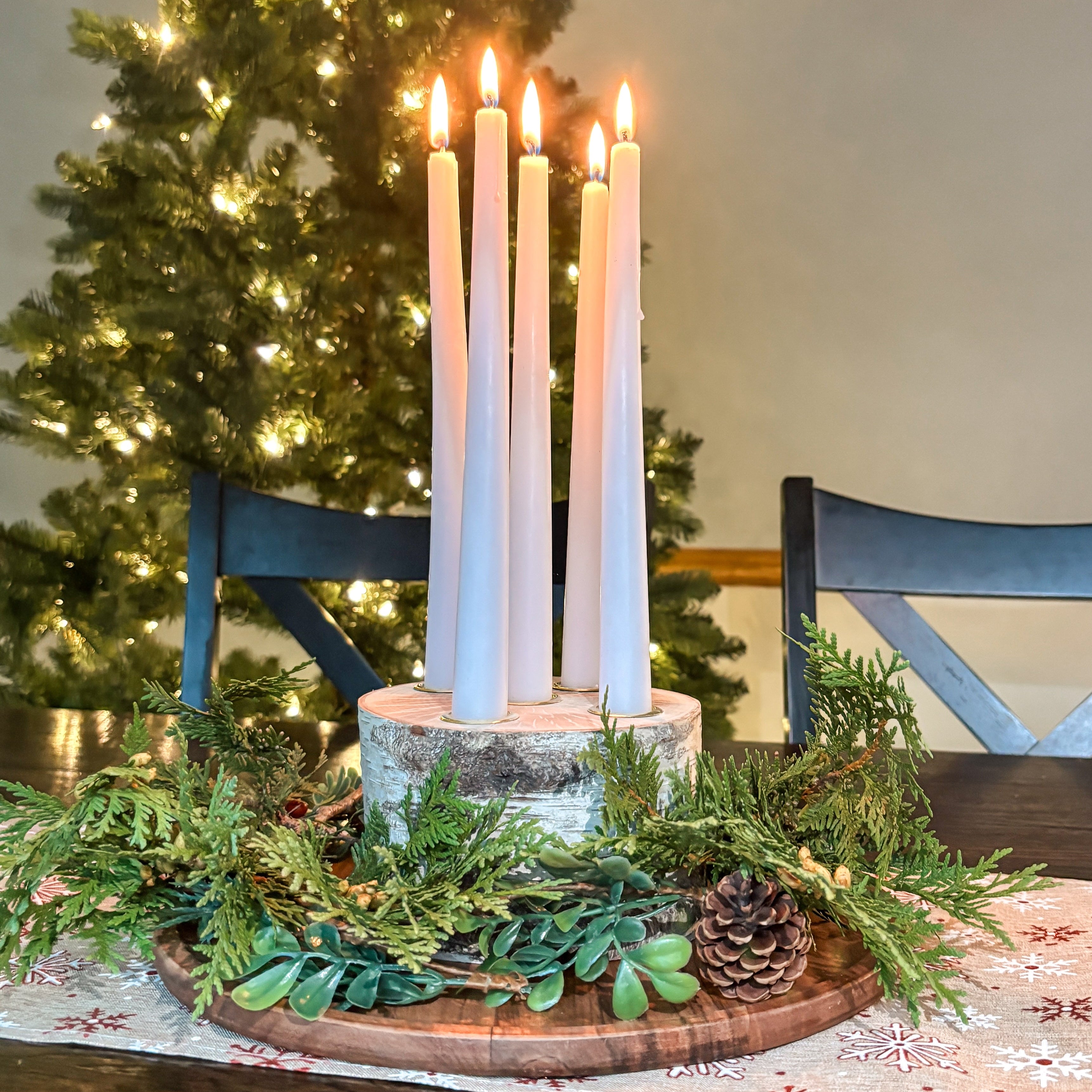 Decorative table setting with candles and greenery in front of a Christmas tree.
