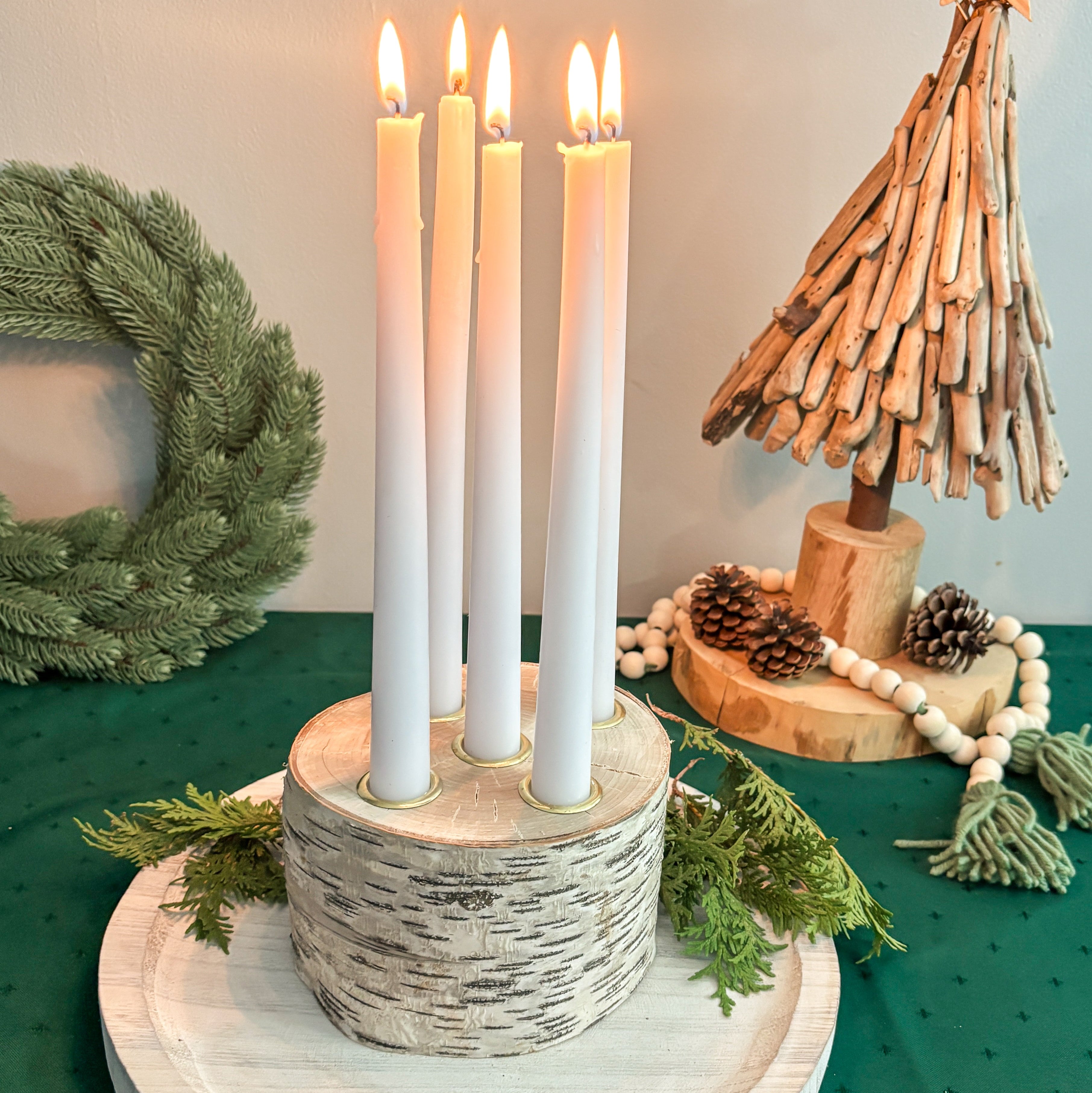 Decorative setup with candles, wreath, and small tree on a green surface
