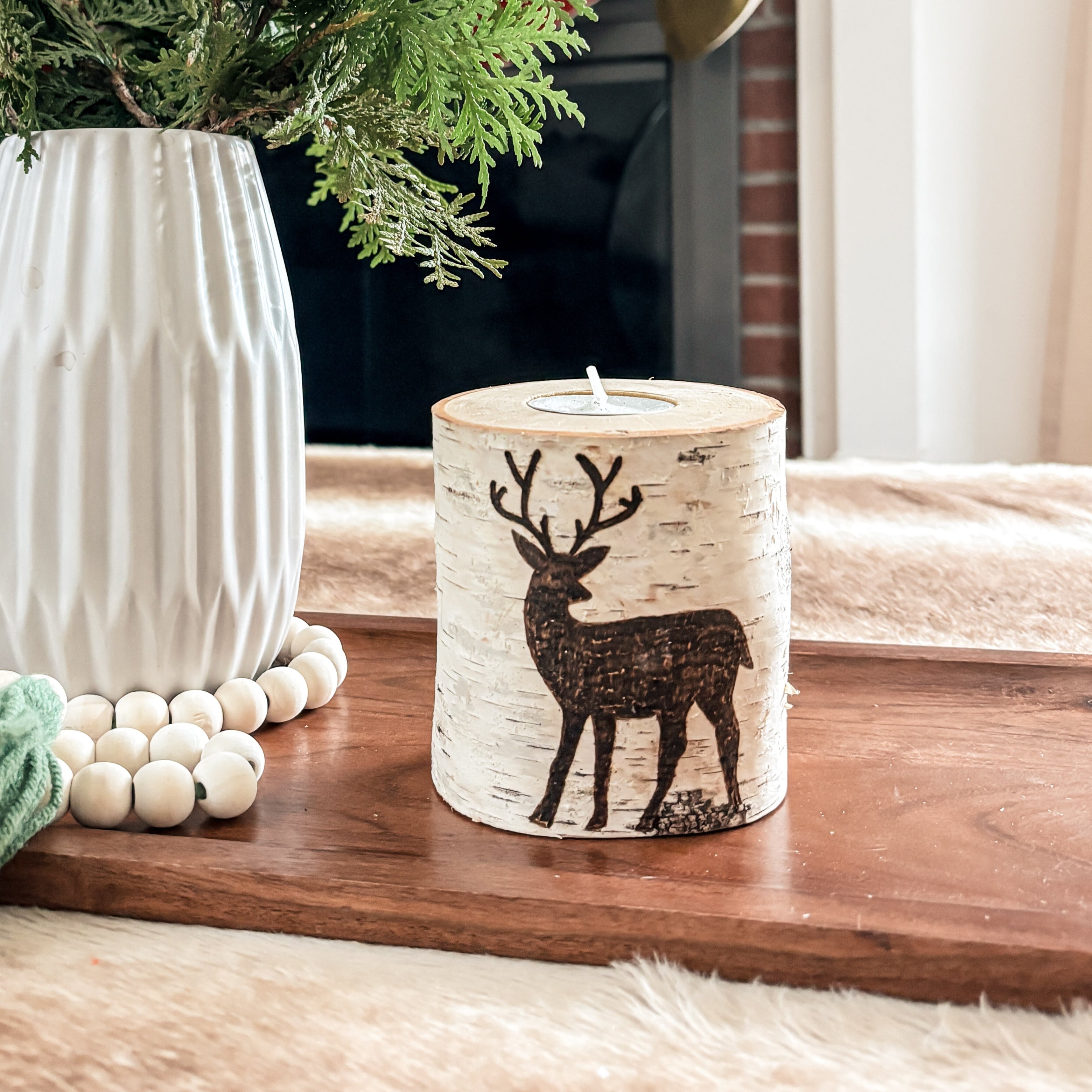 Decorative setup with a vase, candle, and greenery on a wooden table in a cozy room with a Christmas deer birch candle

