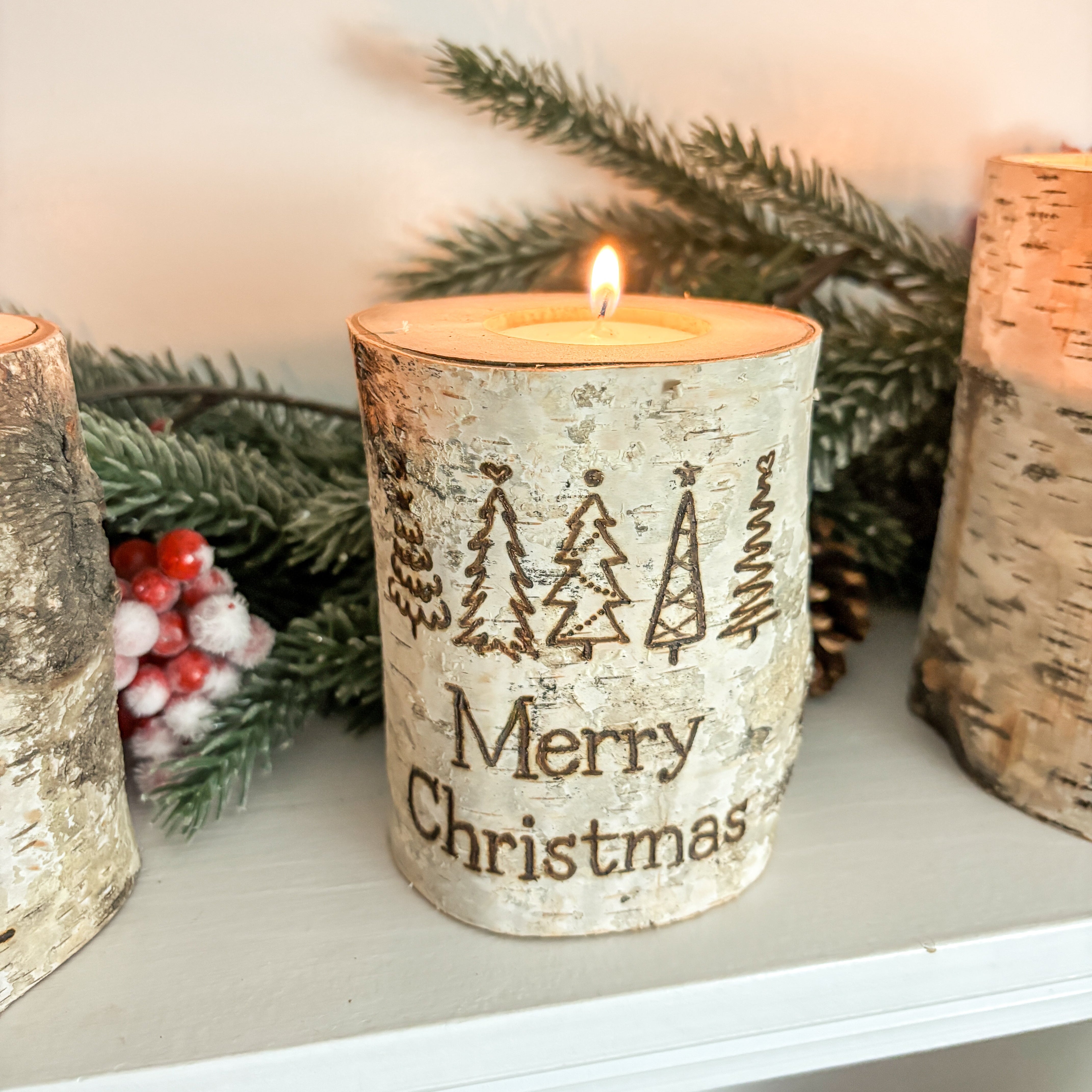 Decorative candle with 'Merry Christmas' text in a birch bark design, surrounded by festive elements.