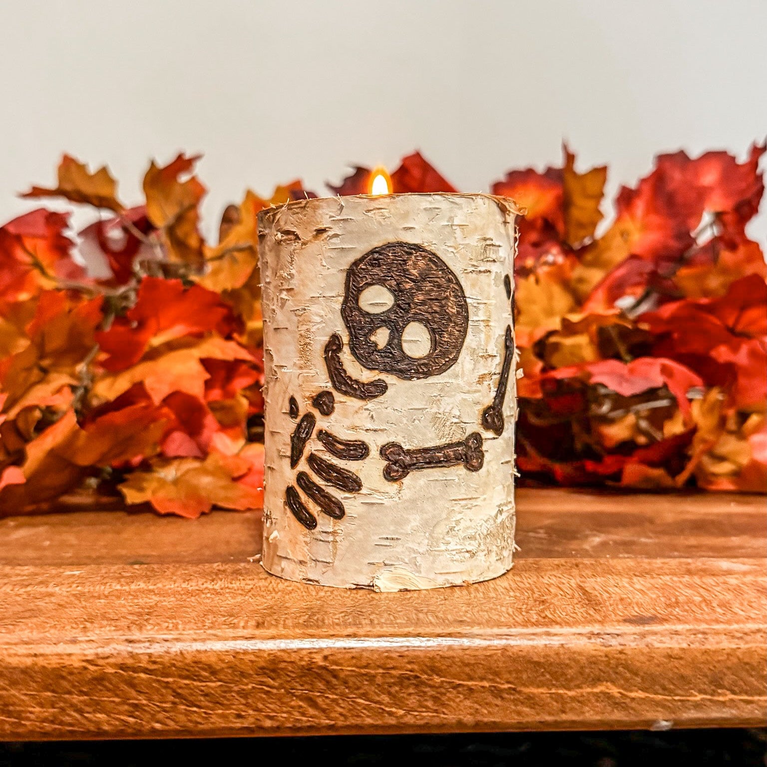 Decorative candle holder with skeleton design on a wooden surface with autumn leaves in the background