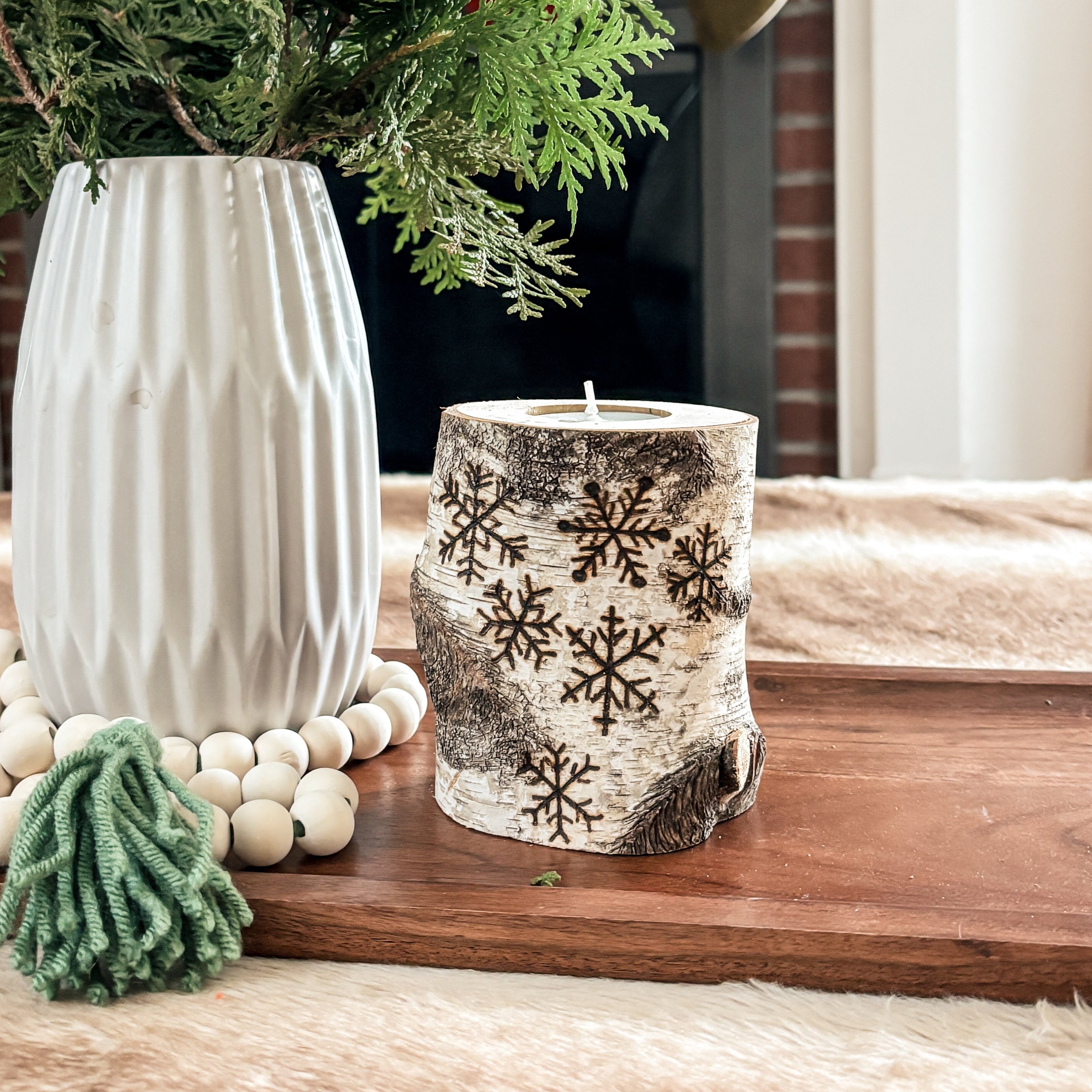 Decorative setup with snowflake birch wood candle holder, a vase, candles, and greenery on a wooden surface.
