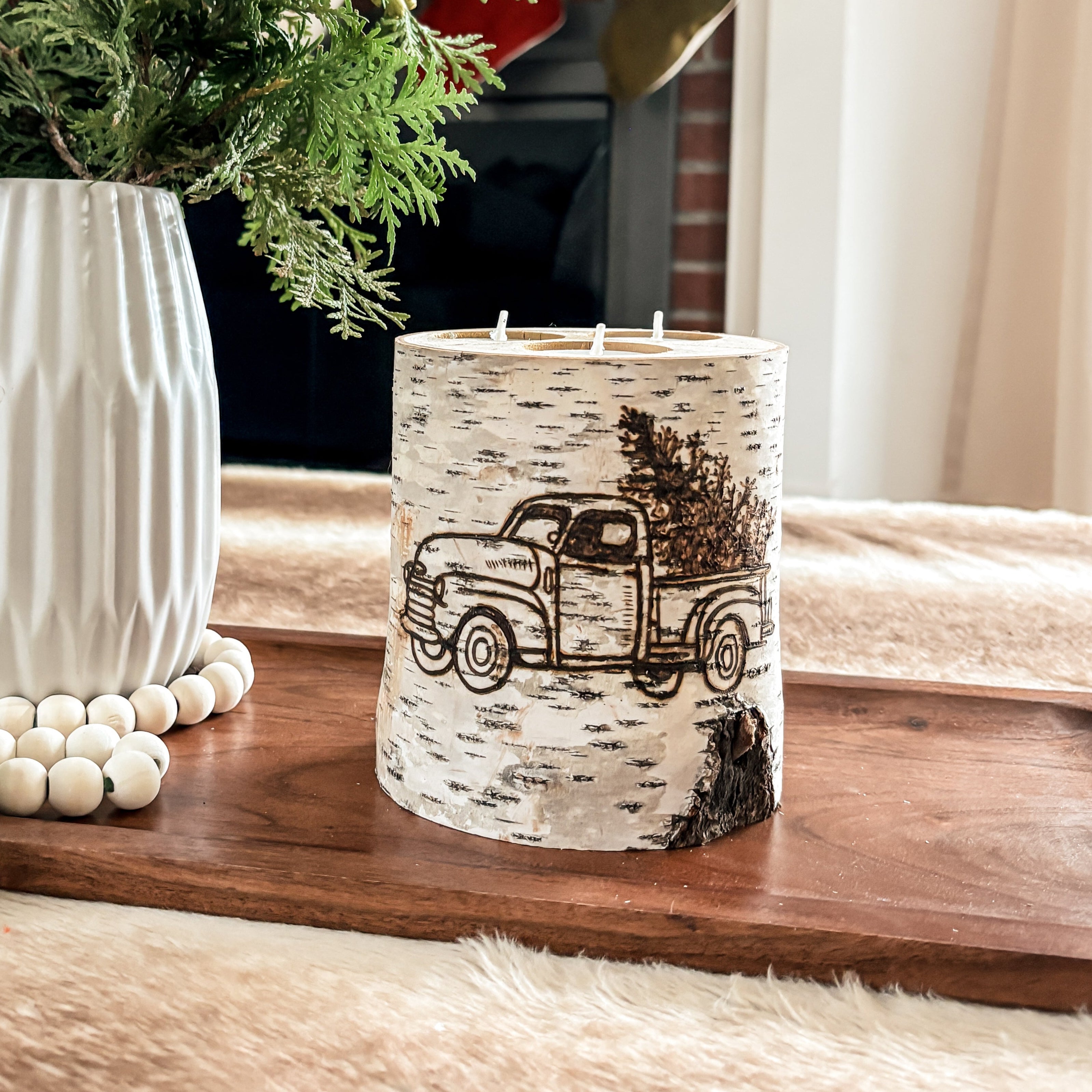 Decorative candle with truck design and vase with greenery on a wooden surface.